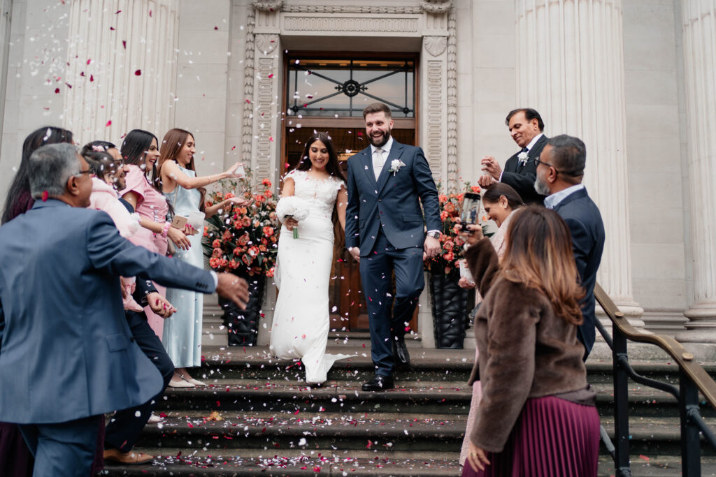 Newlywed couple leaving Marylebone Town Hall after their London wedding ceremony surrounded by confetti.